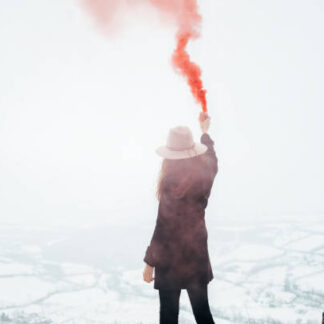 Hipster girl with red smoke bomb send smoke signal. Emergency flare signal.